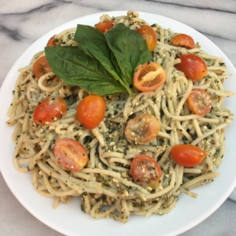 Gluten-free pasta with pesto sauce, tomatoes, and basil