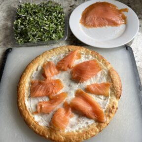 Making gluten-free smoked salmon brunch pizza with cream cheese and micro greens