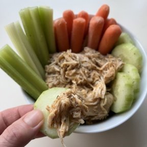 Dipping gluten-free Slow Cooker Buffalo Chicken with cucumber slices